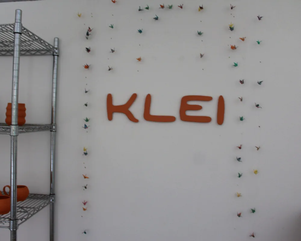 The orange KLEI letters on the studio wall among hanging paper cranes