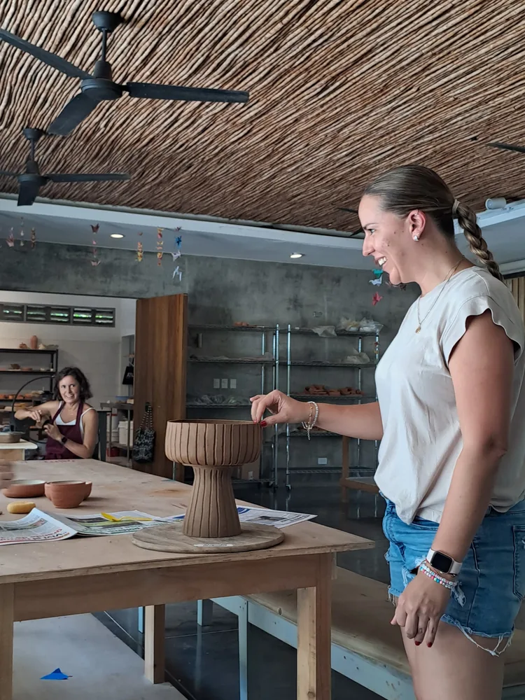 A student smiling at her carved clay vessel at the Klei worktable