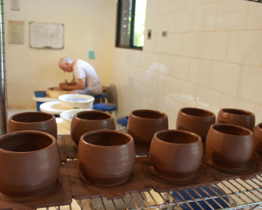 Freshly thrown cups drying on a shelf while Zev works at the wheel