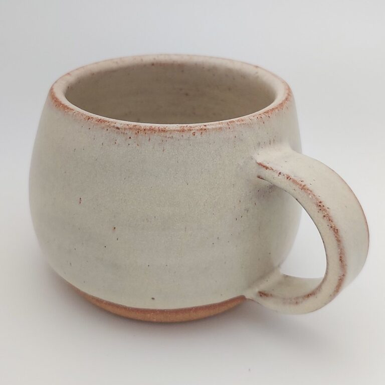 A round white mug with a speckled terracotta rim, made at Klei