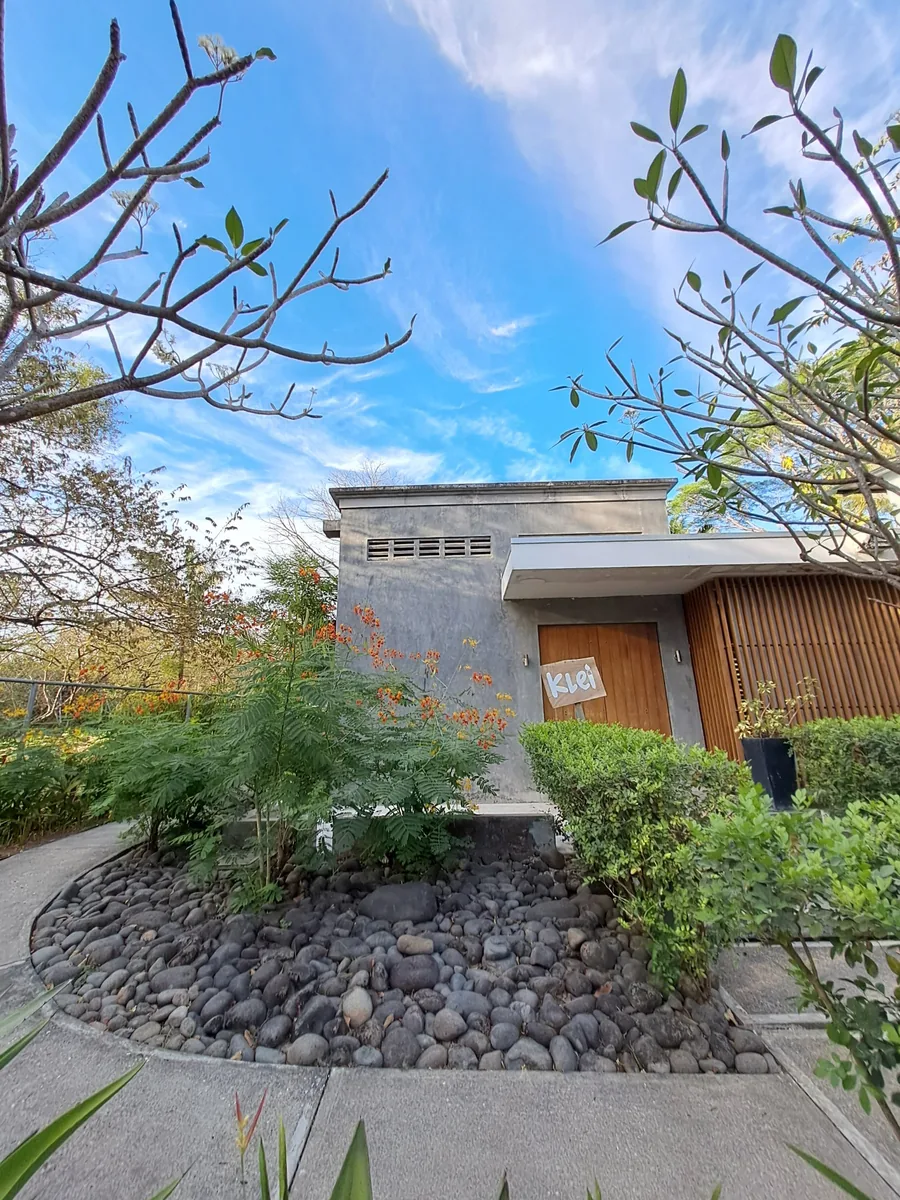 The Klei studio door and sign among flowering plants and river stones in Nosara