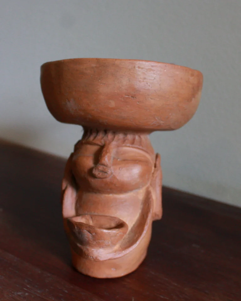 A bisque-fired clay face holding a bowl on its head