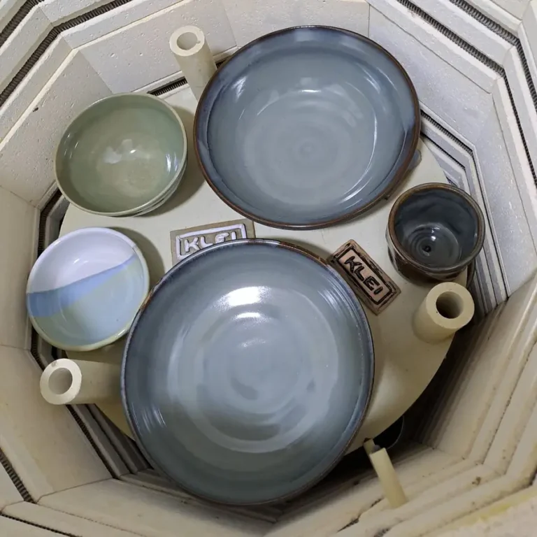 Freshly glazed bowls and cups stamped with the Klei logo inside the kiln