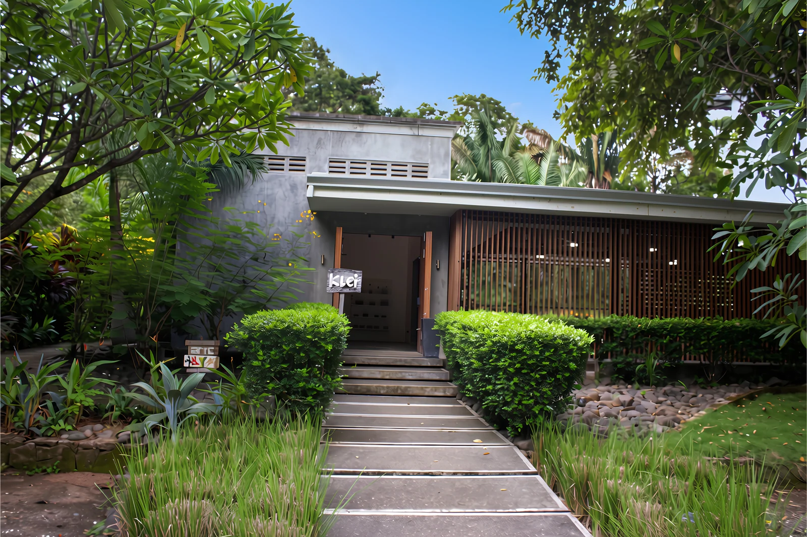The Klei studio entrance in Nosara, with a stone path, green hedges and tropical trees